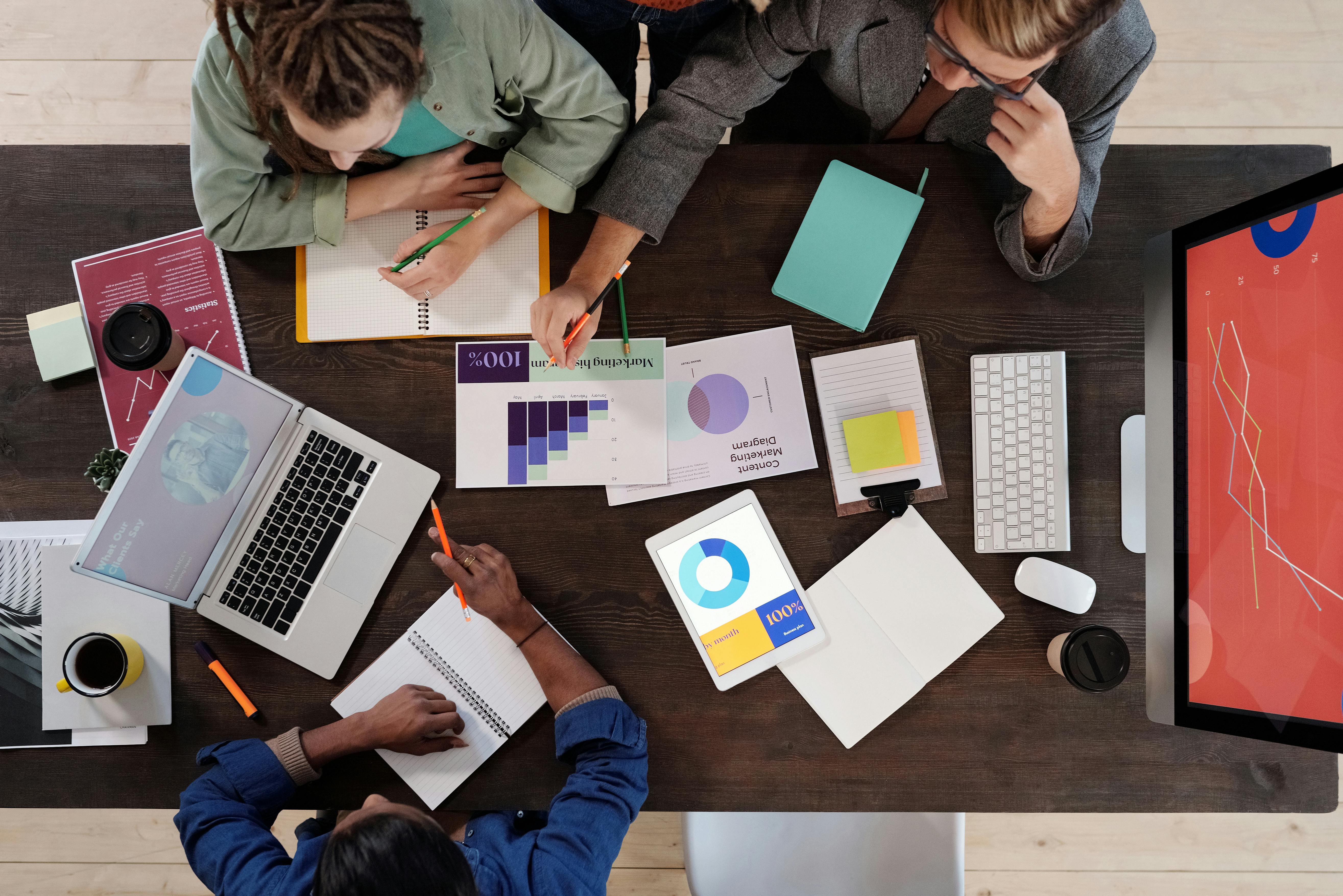 L'image montre des personnes ou des associés d'une entreprise, autour d'une table remplie de documents, en train de se réunir.