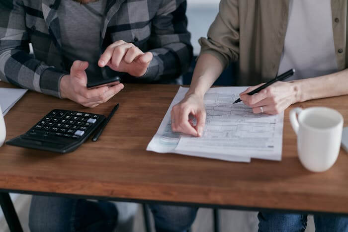 Deux personnes faisant le calcul de leurs charges déductibles en utilisant un téléphone et une machine à calculer.