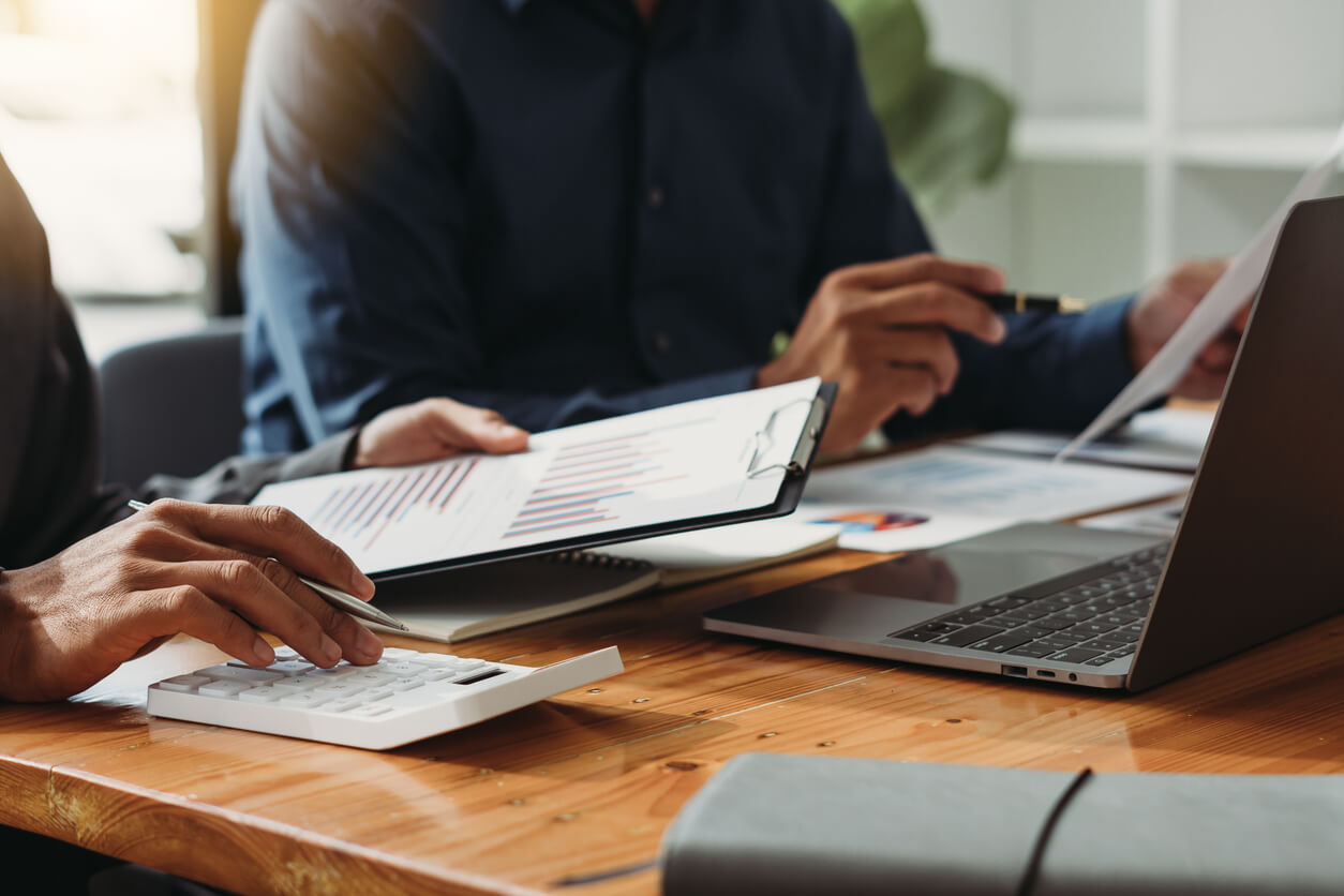 Deux personnes analysant des documents, une calculatrice et un ordinateur pour élaborer un tableau comparatif et décider de créer une SCI à l'IR ou à l'IS.