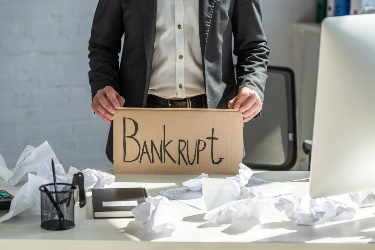 Un homme tenant une pancarte 'Bankrupt' dans un bureau en désordre. L’image illustre la dissolution d'une Société Civile Immobilière suite à des difficultés financières